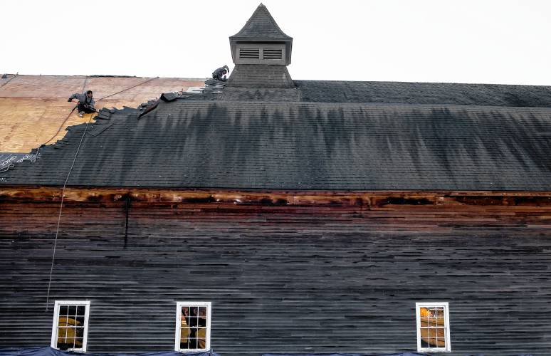 A roofer from Millstone Construction removes old shingles from the Houston Barn at the Hopkinton Library site in Contoocook on Tuesday, January 2, 2024. The worker was attached to two different harnesses as he was removing the roof materials.