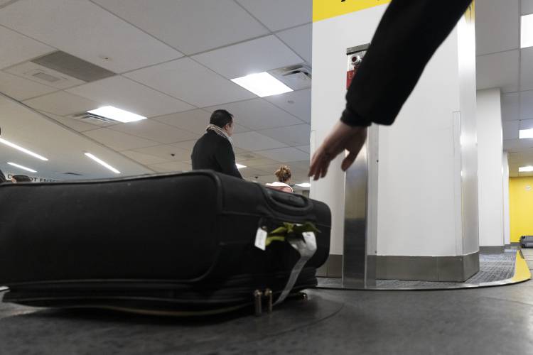 A person retrieves their suitcase from a baggage claim carousel at LaGuardia Airport in New York, Tuesday, Nov. 21, 2023. (AP Photo/Peter K. Afriyie)