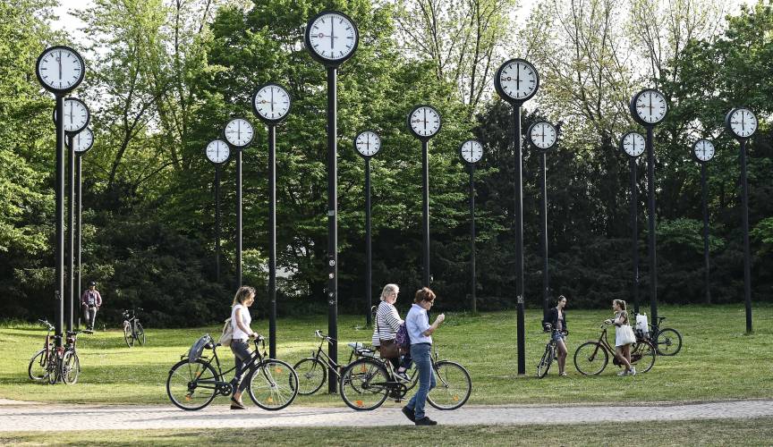 FILE - People with bicycles meet at the clock park in Duesseldorf, Germany, Friday, April 24, 2020. Once again, most Americans will set their clocks forward by one hour this weekend, losing perhaps a bit of sleep but gaining more glorious sunlight in the evenings as the days warm into summer. How we came to move the clock forward in the spring, and then push them back in the fall, is a tale of that spans over a century and is one that's been driven by two world wars, mass confusion...