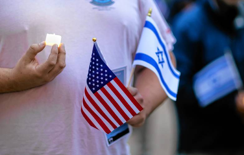A person holds a candle along with the American and Israeli flags during a vigil at the State House in downtown Concord on Monday evening, October 7, 2024, on the anniversary of the Hamas attack on Israel.