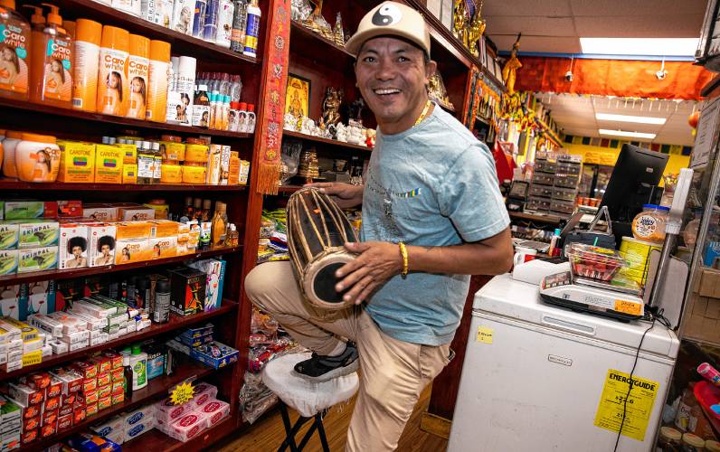 Karma Gonpo takes down drums from a top shelf; Gonpo has the shelves stocked with items that customers will find familiar from their native countries at the Katmandu Bazaar Market on Loudon Road in Concord.