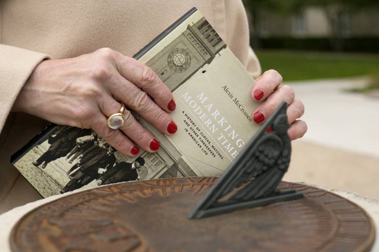 Alexis McCrossen holds a book she authored, Marking Modern Time, in front of a sun dial, as she poses for a photo at Southern Methodist University in Dallas, Wednesday, Feb. 28, 2024. McCrossen, a history professor at SMU, has written books on marking time. (AP Photo/Tony Gutierrez)