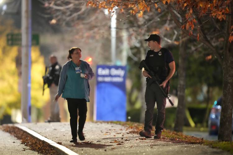A passer-by walks past law enforcement officers carring rifles outside Central Maine Medical Center during an active shooter situation, in Lewiston, Maine, Wednesday, Oct. 25, 2023. (AP Photo/Steven Senne)