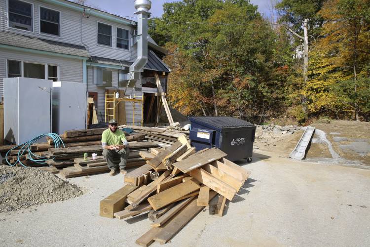 A worker sits outside of a restaurant that is being rebuilt, in Ludlow, Vt., Thursday, Oct. 19, 2023, three months after severe flooding hit the ski town. As winter approaches and the fall tourism season lingers, Ludlow businesses who lost out on summer tourism want to get the word out that they are open, even though a handful are still in the throes of rebuilding. (AP Photo/Lisa Rathke)