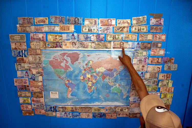 Karma Gonpo points to all the money people have pinned to the wall from their native countries at the Katmandu Bazaar Market on Loudon Road in Concord.