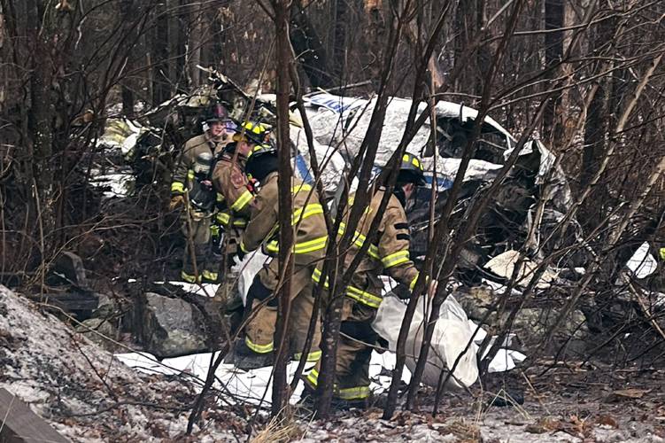 In this photo provided by Eddie Saktanaset, firefighters recover items from the site of a small plane crash, at rear, in a wooded area behind his home, Friday, Jan. 26, 2024, in Londonderry, N.H. The Wiggins Air Beechcraft 99, which was flying light cargo to Maine, crashed about 7:30 a.m. near the Manchester-Boston Regional Airport shortly after takeoff. Firefighters helped remove the trapped pilot, who was taken to a hospital, authorities said Friday. (Eddie Saktanaset photo via...