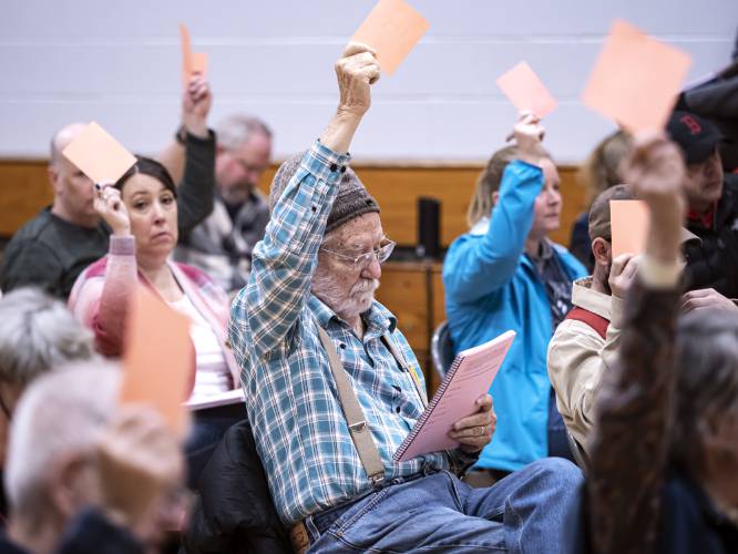 Chichester resident Doug Hall raises an orange card in approval of a warrant article as he starts to read up on the next article at the town meeting at the elementary school on Saturday morning, March 12, 2022.