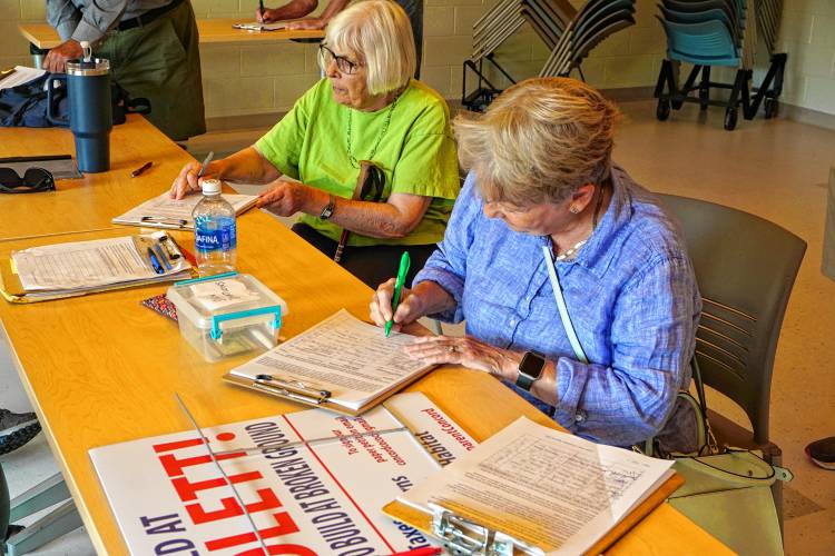 Sue Hofmann, front, signing the Concord Concerned Citizens petition for a ballot question that would give voters power over where Concord puts its schools. Hofmann left the event with several “Rebuild at Rundlett” lawn signs tucked under her arm.