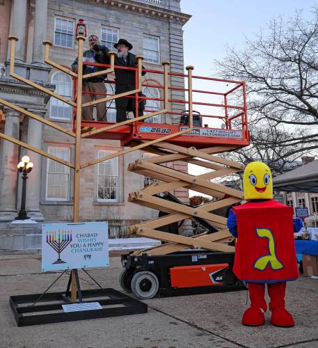 Rabbi Levi Krinsky, regional director of Chabad of New Hampshire and Scott Plaut of Nashua, kindle the 13-foot Menorah in front of the State House marking the first night of Hanukkah. Hanukkah is celebrated for eight days with an additional candle lit each night.