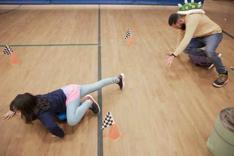 Bailey Flood, 8, races Penacook Elementary School assistant prinicipal Zach Stephenson during a Mario cart race in the school gymnasium on Thursday, March 27, 2025. The Mario Brothers-themed Escape Room included the whole school where students and their families solved mysteries in classrooms and had pizza as well.