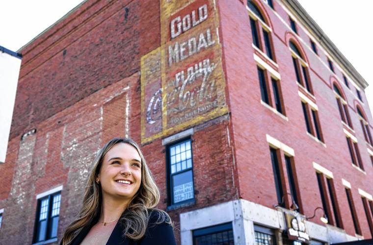 Emily Ricard, a Boscawen native and 2014 graduate of Merrimack Valley High School, stands in front of one of the Gold Medal Flower ghost signs on the side of Phenix Hall in downtown Concord on Friday, March 8.
