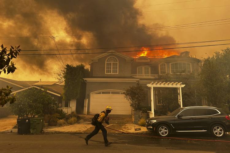 A residence burns as a firefighter battles the Palisades Fire in the Pacific Palisades neighborhood of Los Angeles Tuesday, Jan. 7, 2025. (AP Photo/Eugene Garcia)