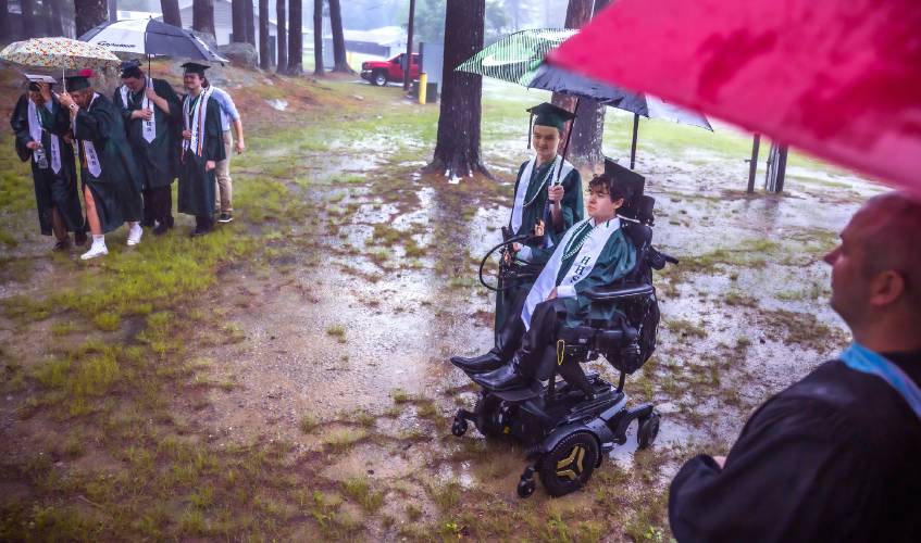 Hopkinton High classmate and friend Teddy Ehrmanntraut holds an umbrella for Constantine Salce as they make their way through the pouring rain to the 'barn' at the Hopkinton High School graduation on Friday, June, 6, 2025.