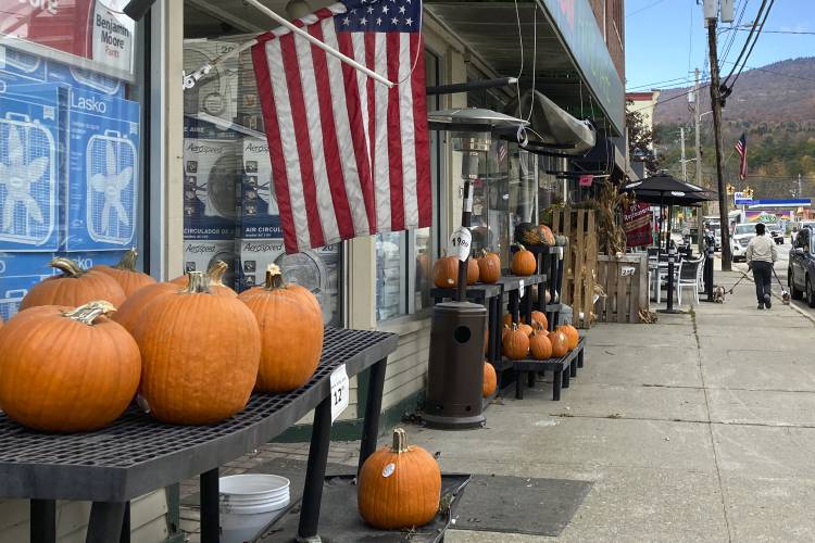 Pumpkins rest on shelves in front of a store on Main Street, Thursday, Oct. 19, 2023, in Ludlow, Vt., three months after severe flooding hit the ski town. As winter approaches and the fall tourism season lingers, Ludlow businesses who lost out on summer tourism want to get the word out that they are open, even though a handful are still in the throes of rebuilding. (AP Photo/Lisa Rathke)