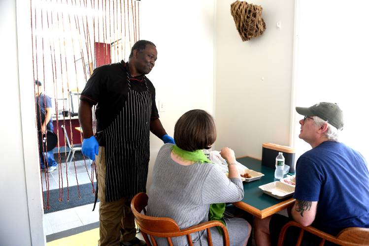 Cheryl Junker and husband Josh Macomson, of Canaan, sit down for their first meal at The Karibbean on Friday in West Lebanon. Owner Balvin Bowen checks on the couple after they are served. The couple said they were very excited to have good Jamaican food in the area.