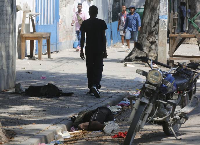 A lifeless body lies against the curb as pedestrians walk past in Port-au-Prince, Haiti, Monday, March 11, 2024. (AP Photo/Odelyn Joseph)