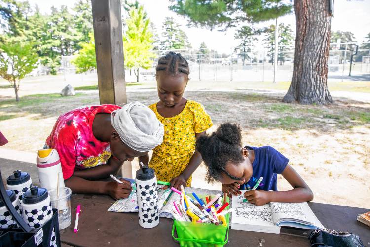 Rowayda Eldoud, left, her sister, Enus, and friend Doreen Uwase draw in their coloring books underneath a covered picnic table at Keach Park as part of the Project STORY program on Thursday.