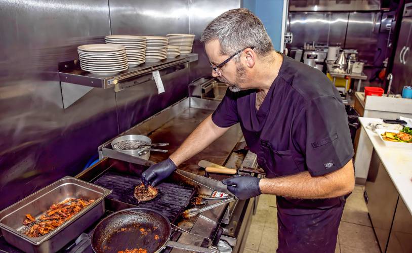 Scott Partridge prepares a blue cheese bacon burger with fries to go at the grill at the Friendly Diner in Pittsfield.