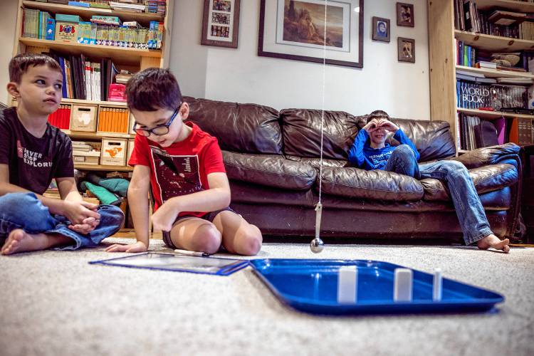 Ryan LeGeyt, left, watches his brother, Greyson, work on an addition game as brother, Bryce, sits on the couch at their home.