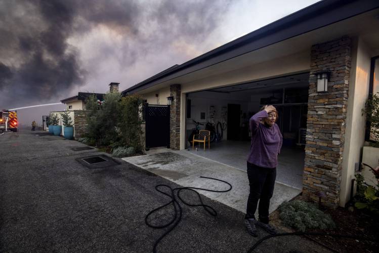 A resident stands in front of a garage as fire crews fight the Palisades Fire nearby in the Pacific Palisades neighborhood of Los Angeles, Tuesday, Jan. 7, 2025. (AP Photo/Ethan Swope)