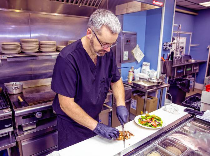 Scott Partridge prepares a chicken in a salad to go at the grill at the Friendly Diner in Pittsfield.