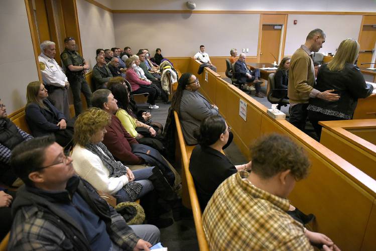 YDC victim Michael Gilpatrick stands with his wife, Kelly, at right, as she reads the victim's statement at the sentencing hearing for Bradley Asbury, 70, at Hillsborough County Superior Court in Manchester, N.H., Monday, Jan. 27, 2025. (David Lane/Union Leader via AP, Pool)