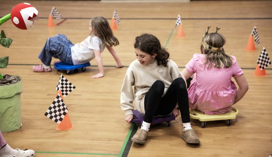 Molly Rudis (center) and sisters Sophie and Caitlyn Kleiner run in the Mario cart race in the Penacook Elementary School gym during the Escape Room family engagement night at the school on Thursday, March 27, 2025.