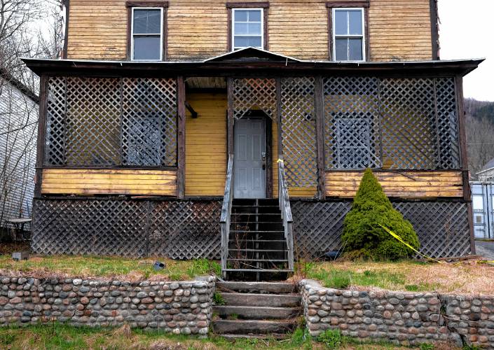 A padlock seals the door at the yellow shingled house Western Avenue in Berlin, New Hampshire. Rotten wood frames a broken window along the side and spray painted letters on the garage read ‘stay out.’