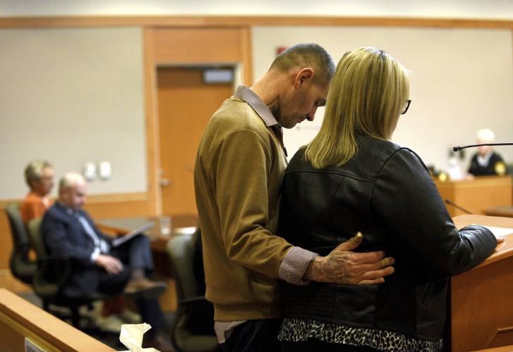YDC victim Michael Gilpatrick stands with his wife, Kelly, at right, as she reads the victim's statement at the sentencing hearing for Bradley Asbury, 70, at Hillsborough County Superior Court in Manchester, N.H., Monday, Jan. 27, 2025. (David Lane/Union Leader via AP, Pool)