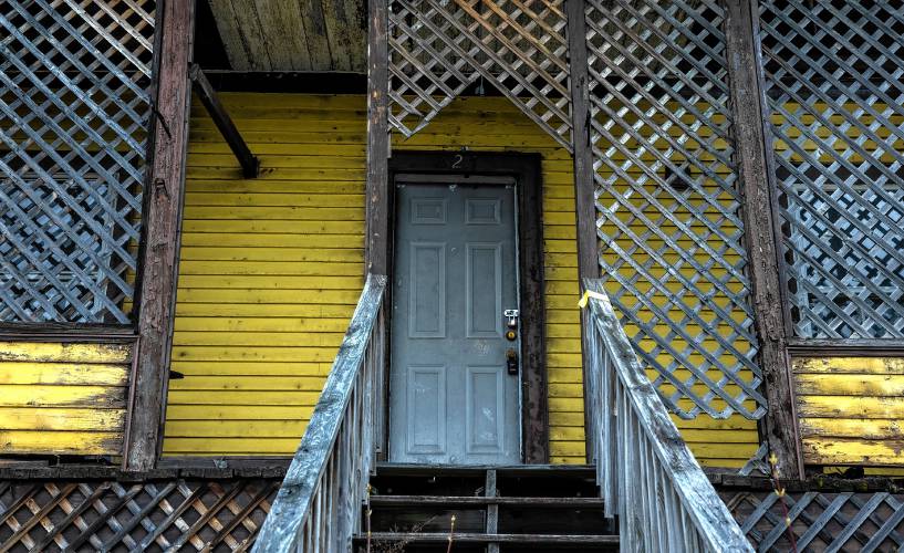 A padlock seals the door at the yellow shingled house Western Avenue in Berlin, New Hampshire. Rotten wood frames a broken window along the side and spray painted letters on the garage read ‘stay out.’