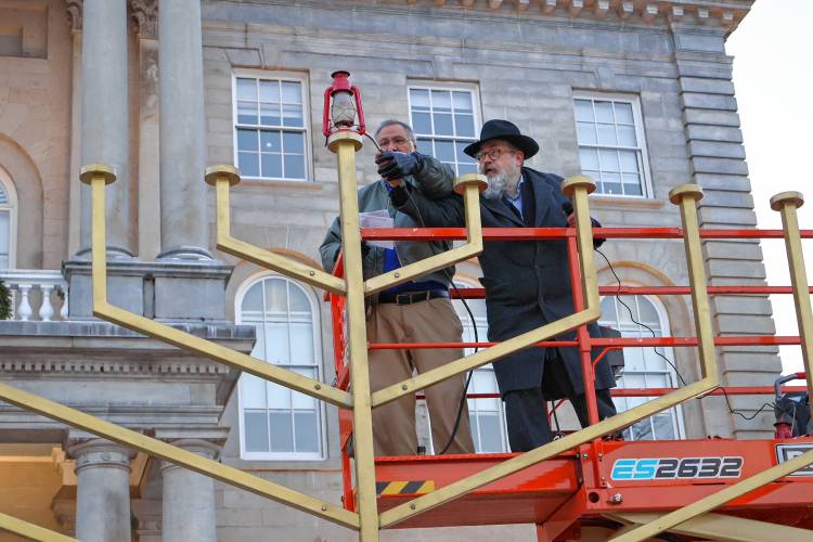 Rabbi Levi Krinsky, regional director of Chabad of New Hampshire, and Scott Plaut of Nashua kindle the 13-foot Menorah in front of the State House marking the first night of Hanukkah. Hanukkah is celebrated for eight days with an additional candle lit each night.