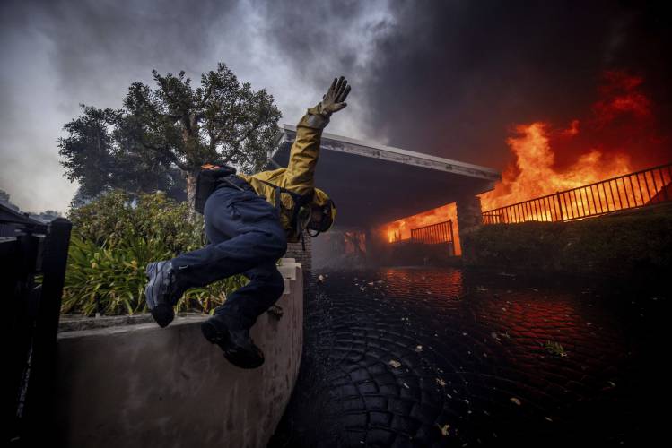 A firefighter jumps over a fence while fighting the Palisades Fire in the Pacific Palisades neighborhood of Los Angeles, Tuesday, Jan. 7, 2025. (AP Photo/Ethan Swope)