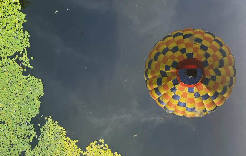 The reflection of a hot air balloon in the water seen from above as it floats over Pittsfield.