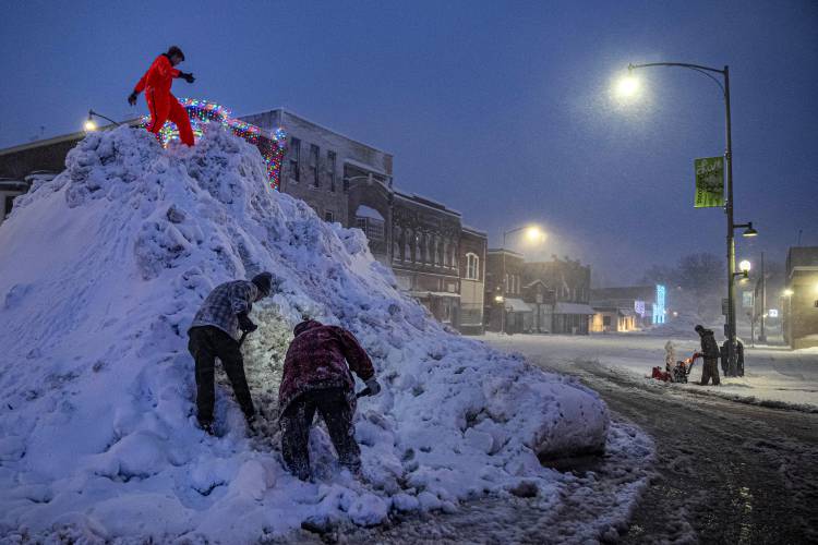 People stand on a large snow pile in Oskaloosa, Iowa, Tuesday, Jan. 9, 2024, as another person uses a snow blower . (AP Photo/Andrew Harnik)