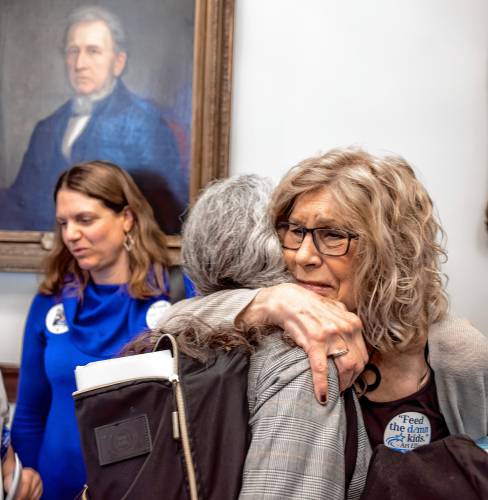 Sally Varney gets a hug from her friend, Rep. Muriel Hall outside the House gallery before the session that honored her partner, Art Ellison on Thursday morning, April 11, 2024. Ellison’s daughter, Anna Bates is in the background. Varney and Bates were given stickers that said, ‘Feed the damn kids.’