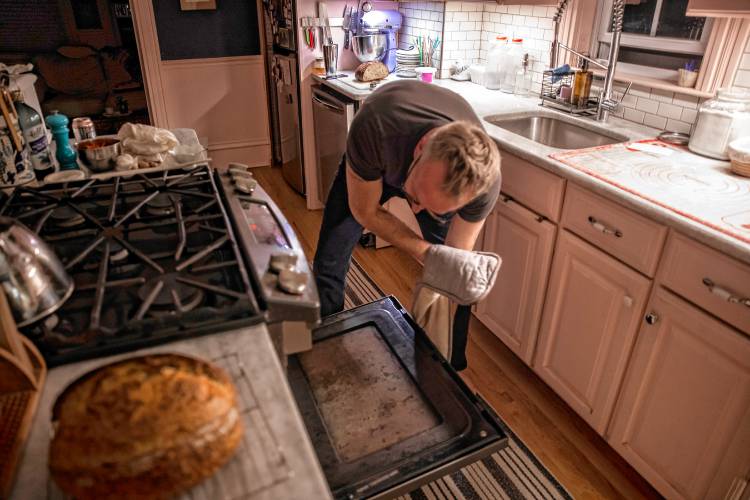 Alex Brown puts the dough for his bread into the oven at his South End home. Brown is getting a new bread oven to increase his weekly output.