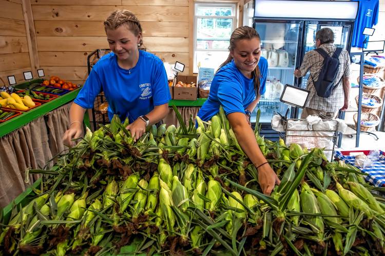 Workers Sammy Baker (left) and Macy Gordon from Highway View Farm in Boscawen arrange the fresh corn at the farm stand on Route 4.