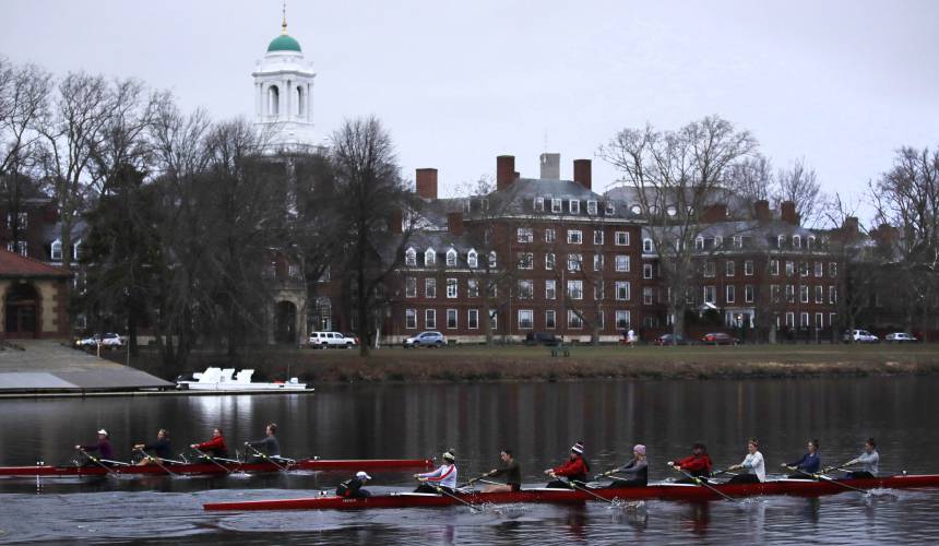 Rowers pass the campus of Harvard University as they paddle down the Charles River in Cambridge, Mass.