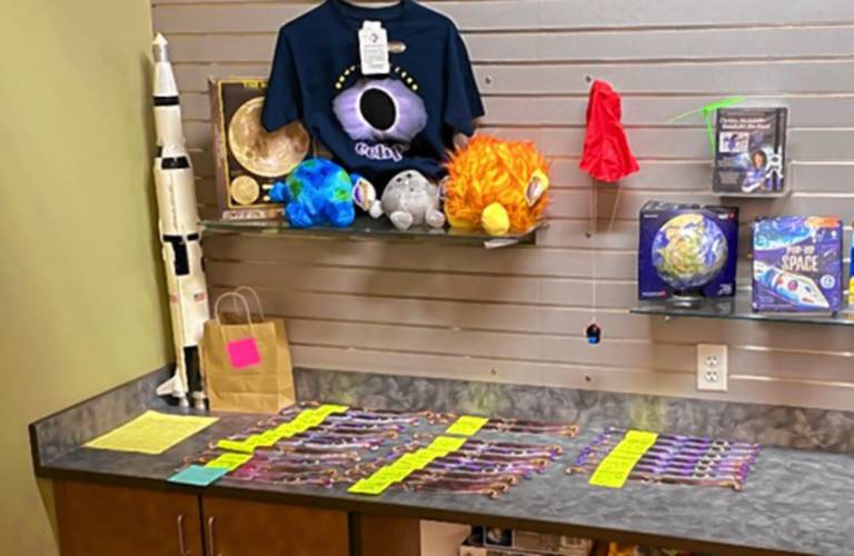 Dozens of pre-ordered eclipse glasses can be seen behind the counter of the McAuliffe-Shepard Discovery Center gift shop, waiting to be picked up. 