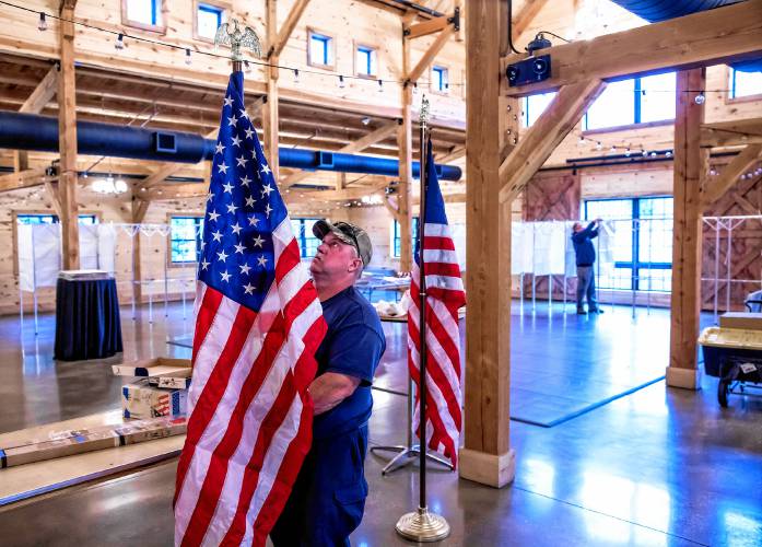 Concord Public Properties crew member Mike Pickering sets up the American flags inside The Barn at Bull Meadow on Bog Road as the crews prepared for the Ward Two voting place on Monday, Nov. 4, 2024. 