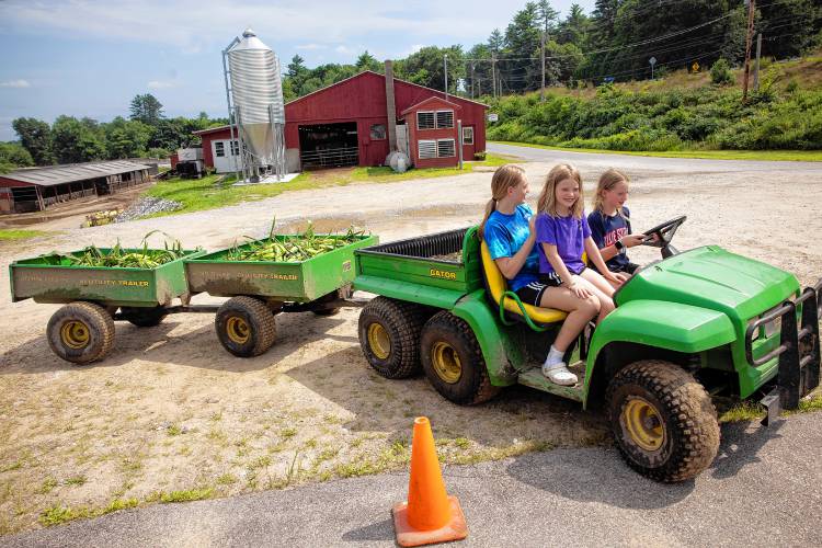 Lucy, (driving), Abby, and Julie Crete drive the ATV at  the family Highway View Farm in Boscawen delivering just-picked sweet corn to the farmstand off of Route 4 on Monday, August 5, 2024.