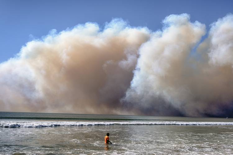A swimmer watches as a large dark plume of smoke passes over the beach from a wildfire from Pacific Palisades, in Santa Monica, Calif., Tuesday, Jan. 7, 2025. (AP Photo/Richard Vogel)