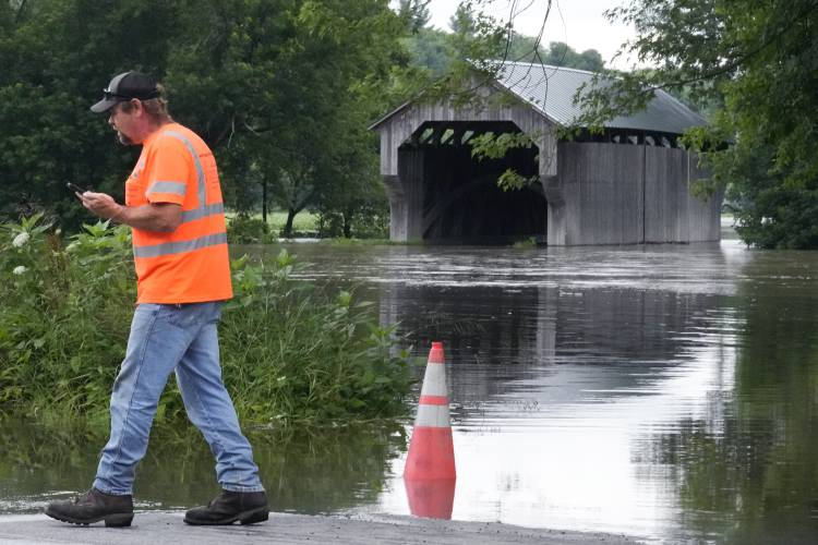 Jody Tanner, of the Vermont Transportation Agency, talks with co-workers at a high water point of the Lamoille River along Route 15 after remnants of Hurricane Beryl caused flooding, Thursday, July 11, 2024, in Cambridge, Vt. At rear is the Gates Farm Covered Bridge. (AP Photo/Charles Krupa)