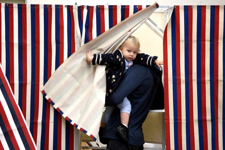 Kylie Copp peeks out from the voting booth where her father Corey Copp votes in Canaan on Tuesday.