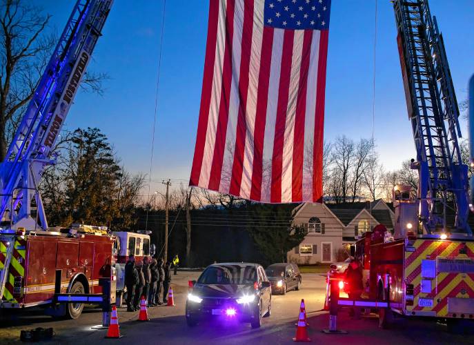 The funeral procession for former Franklin Police Chief Bradley Haas passes under an American flag in the parking lot of Winnisquam High School for his funeral service on Monday.
