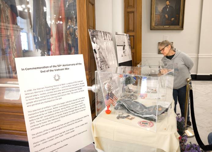 Gail Gordon looks over the Vietnam War 50th Anniversary display that is displayed in the New Hampshire State House Hall of Flags on the day the Vietnam War came to end.