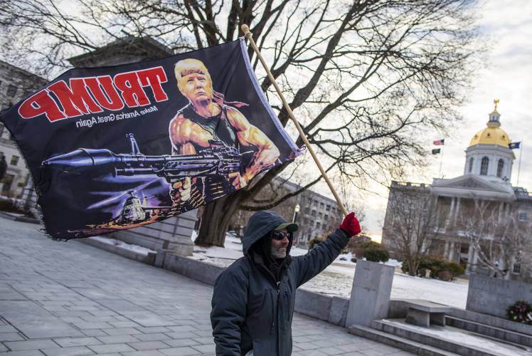 A flag with President Donald Trump holding a rocket launcher as a Rambo figure is seen in front of the New Hampshire State House in 2020. A flag with President Donald Trump holding a rocket launcher as a Rambo figure is seen in front of the New Hampshire State House in 2020.