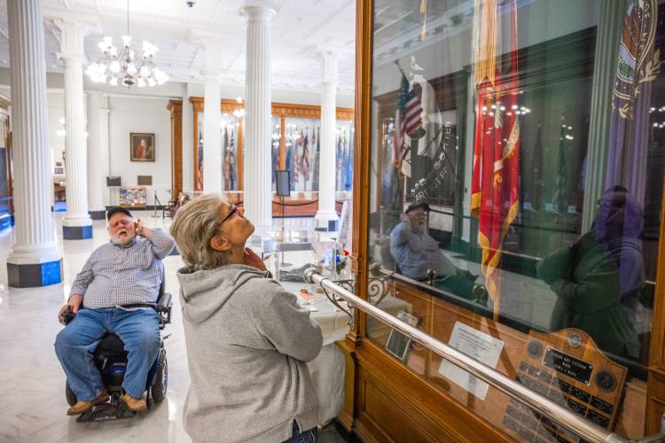Gail Gordon gazes up at the DAV flag that her husband, Gary, placed in the Hall of Flags at the State House on Wednesday, April 30, 2025. This display marks the 50th anniversary of the end of the Vietnam War.