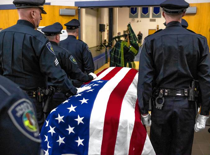 Franklin police officers put their hands on the casket of Former Police Chief Bradley Haas before entering the service in his honor at Winnisquam High School on Monday, November 27, 2023.