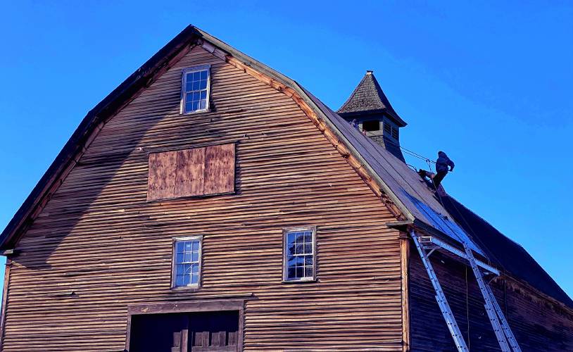 A roofer from Millstone Construction removes old shingles from the Houston Barn at the Hopkinton Library site in Contoocook on Tuesday.